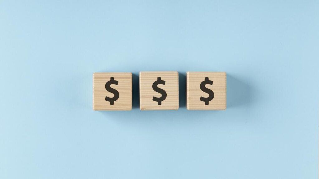 Dollar signs embossed on small wooden cubes.